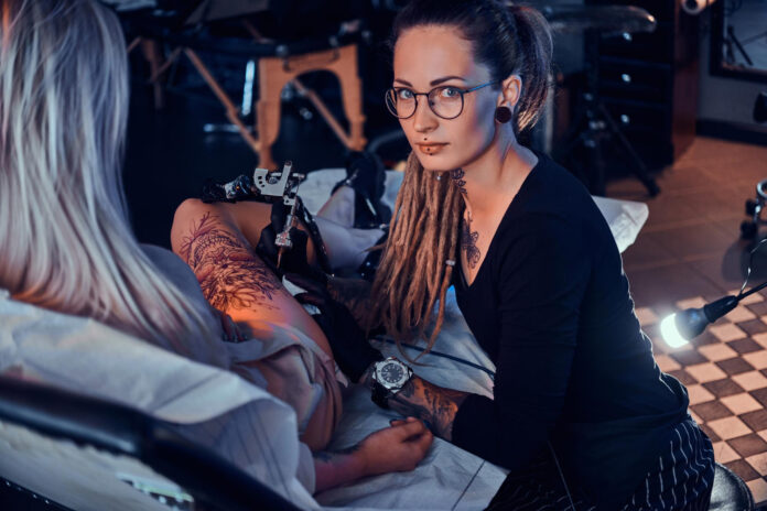 beautiful creative master with dreadlocks is working new peace big leg tattoo customer