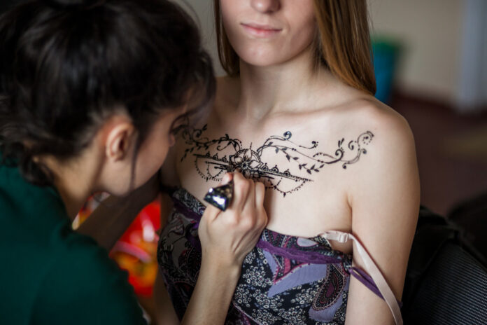 female artist drawing mehndi tattoo woman s chest