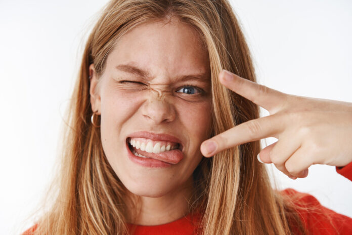 headshot funny emotive charismatic young carefree woman making faces sticking out tongue showing peace gesture winking expressing positive excited emotions posing grey wall headshot funny emotive charismatic young carefree woman making faces sticking out tongue showing peace gesture winking expressing positive excited emotions posing grey wall