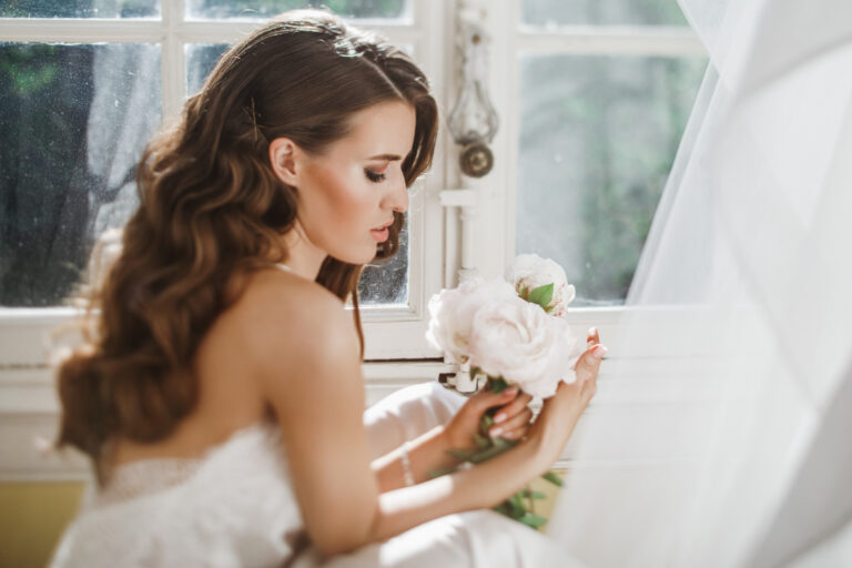 young bride holds bouuqet peonies siting windowsill bright morning