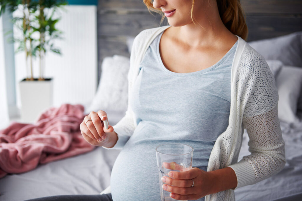 young pregnant woman taking capsule