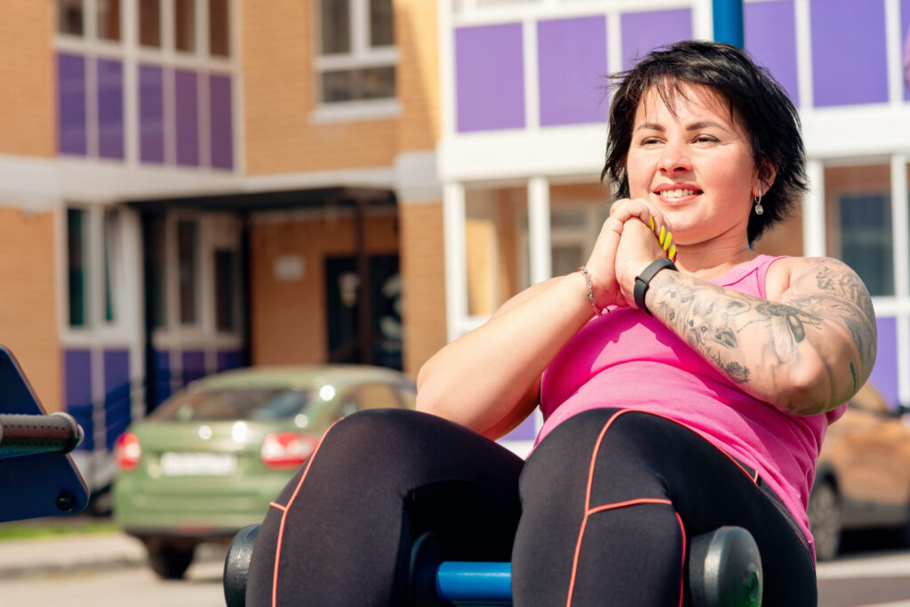 young woman performing abdominal exercises using outdoor exercise machine sit up bench
