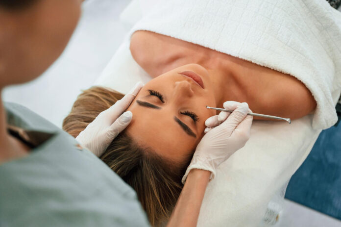 using cosmetic spoon woman face getting facial care by beautician hands spa salon