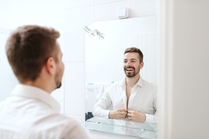 smiling,handsome,businessman,dressing,up,for,work,while,standing,in