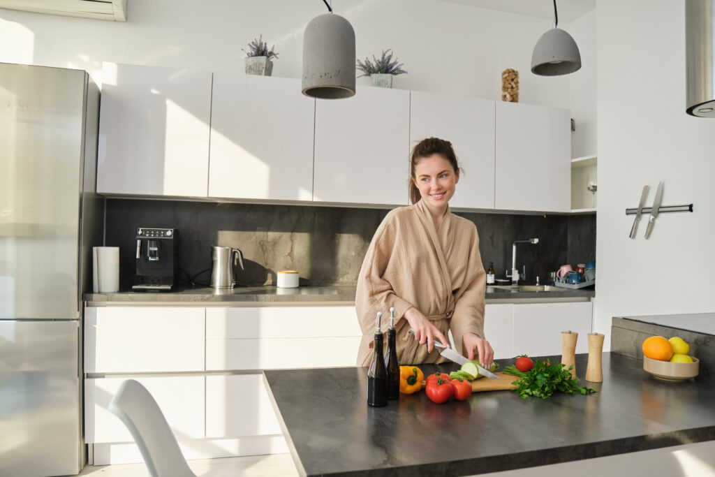 portrait of good looking woman cooking salad in the kitchen, chopping vegetables and smiling, preparing healthy meal, leading healthy lifestyle and eating raw food